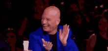 a bald man in a blue suit is smiling and clapping in front of a crowd .