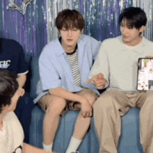 a group of young men are sitting on a couch and one is holding a tablet .