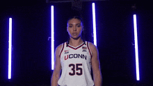 a woman in a uconn basketball jersey is standing in front of a basketball hoop .