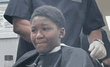 a young boy is getting his hair cut by a man wearing gloves