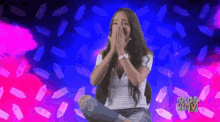 a woman is covering her mouth with her hands in front of a pink and blue background with bottles and the word mtv on it