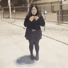 a woman in a black sweater and a purple skirt is standing in the snow