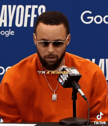 a man wearing sunglasses and a necklace says " i 'm a winner " in front of a nba microphone