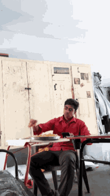 a man in a red shirt is sitting at a table eating food