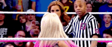 a referee is standing in a wrestling ring with a woman in a pink dress .