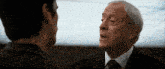 a man in a suit and tie talks to another man in a dark room