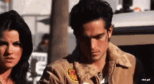 a man and a woman are standing next to each other and the man is wearing a jacket with a patch on it .