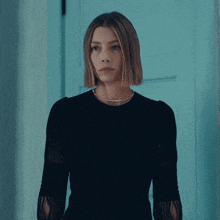 a woman wearing a black top and a gold necklace stands in front of a blue door