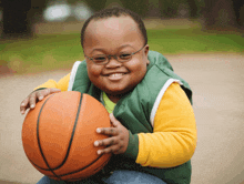 a young boy with glasses holds a basketball and smiles