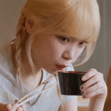 a young woman is eating noodles with chopsticks from a bowl .