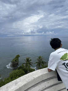 a man wearing a white shirt that says ts on it looks out over the ocean