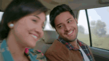 a man and a woman are sitting in the back seat of a car and smiling
