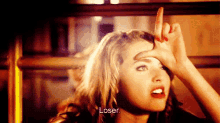 a woman is making a loser sign with her hand on her forehead .