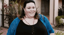 a woman wearing a blue cardigan and a black top is smiling .