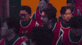 a group of people wearing red and green vests are standing next to each other .
