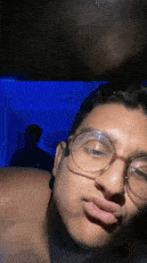 a man wearing glasses looks at the camera with a blue background behind him