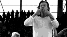 harry styles is wearing a white sweater and covering his mouth with his hands in a black and white photo .
