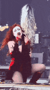 a woman singing into a microphone while another woman holds her hair