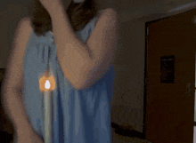 a woman in a blue shirt is holding a candle in her hand