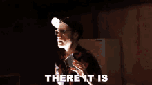 a man with glasses and a hat is holding a piece of glass and saying there it is