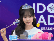 a girl with a tiara on her head holds a wand in front of a sign that says idol season