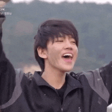 a young man in a black jacket is laughing with his mouth open