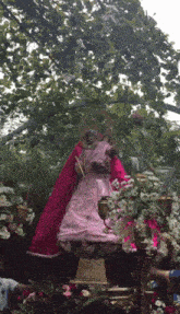 a statue of a woman in a pink dress is surrounded by flowers and candles