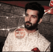 a man with a beard is standing in front of a brick wall with lights hanging from it .