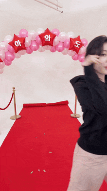 a woman stands on a red carpet in front of a balloon arch that says ' i ' on it