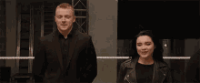 a man in a suit and a woman in a leather jacket are standing next to each other in a wrestling ring .