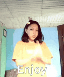 a girl with a flower in her hair is wearing a yellow shirt and says enjoy .