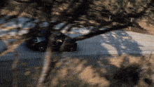 a black car is driving down a road with trees in the foreground