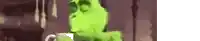 a green parrot is standing in front of a brown wall and looking at the camera .