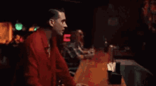 a man in a red shirt is standing behind a bar .