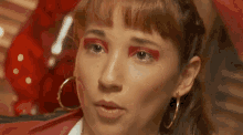 a close up of a woman 's face with red eye shadow and gold hoop earrings