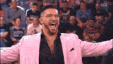 a man in a pink suit and glasses is standing in front of a crowd with his arms outstretched .