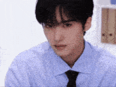 a young man wearing a blue shirt and tie looks at the camera