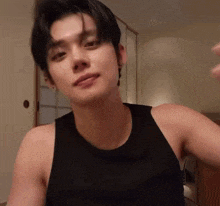 a young man in a black tank top is sitting in a room .
