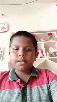 a young boy wearing a red and gray shirt with a clock on the wall behind him that says ' clock '