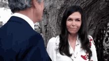 a man in a suit and a woman in a white shirt are standing next to a tree
