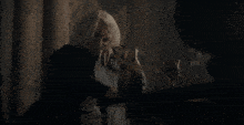 a man with white hair is sitting in a dark room with his head resting on a chair .