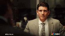 a man in a suit and tie is standing in front of a sign that says nbc