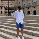 a man in a white shirt and blue shorts stands on a set of stairs in front of a building