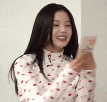 a woman wearing a white shirt with cherries on it is smiling while holding a card .