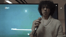 a man with curly hair is holding a microphone in front of a screen that says ' ran ' on it