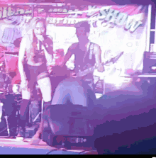 a woman singing into a microphone with a man playing a guitar in front of a sign that says show