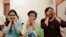 three women covering their eyes with their hands while smiling