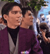 a man in a purple jacket is standing next to another man in a black shirt .