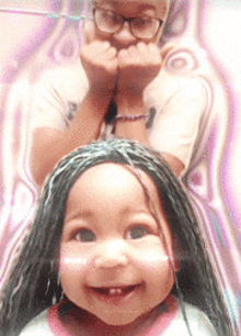 a little girl with braids on her head is smiling with a man behind her