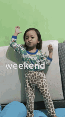 a little girl is standing on a bed with the word weekend written on the bottom